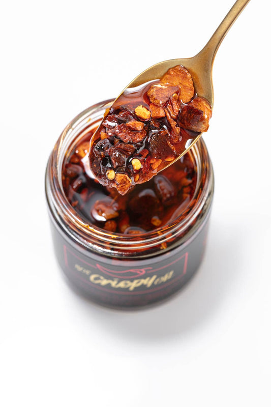 Jar of hot pepper chili  crisp with a spoonful on a white background
