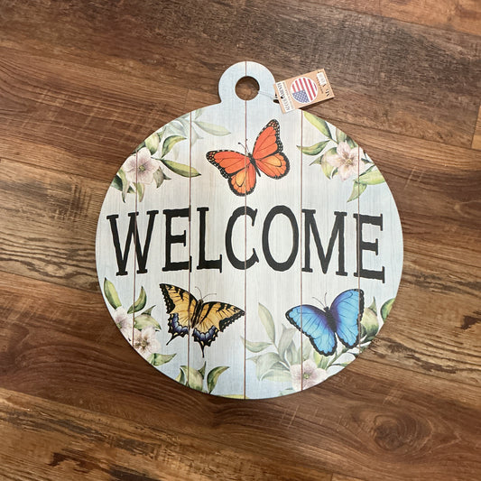 Round wooden sign with 'WELCOME' and butterfly designs on a wooden floor.